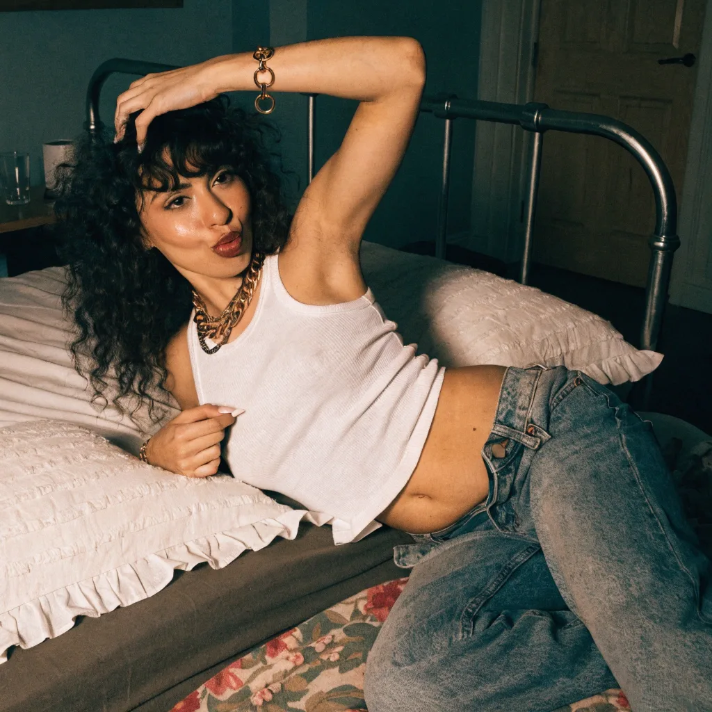 woman in jeans and a tank top posing on a brass bed